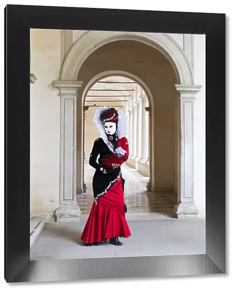 A woman in a red costume and mask poses in an archway during the Venice Carnival