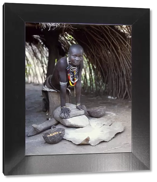A Kwego woman grinds sorghum flour at the entrance to her hut