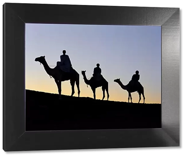 Three camel riders silhouetted against an evening sky