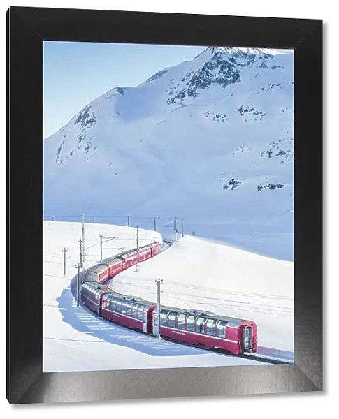 Bernina Express red train passing Lago Bianco in a scenic winter mountain landscape