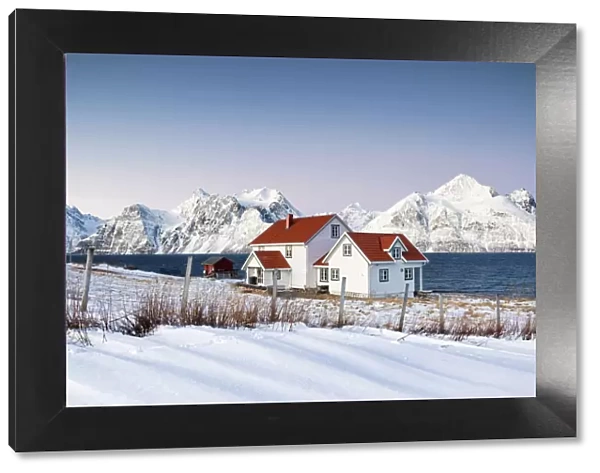 Blue sky on the wooden huts called Rorbu framed by frozen sea and snowy peaks Djupvik