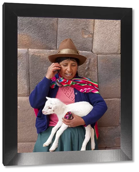 South America, Peru, Cusco. A Quechua woman standing in front of an Inca wall, holding