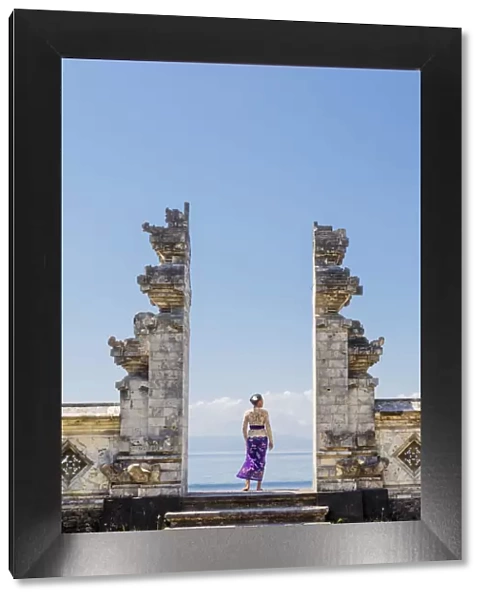 Indonesia, Bali, Candidasa. A local young woman standing in the gateway to the Pura