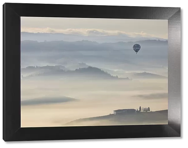 An hot air balloon flies over vineyards and mist during autumn, Cuneo, Langhe e Roero