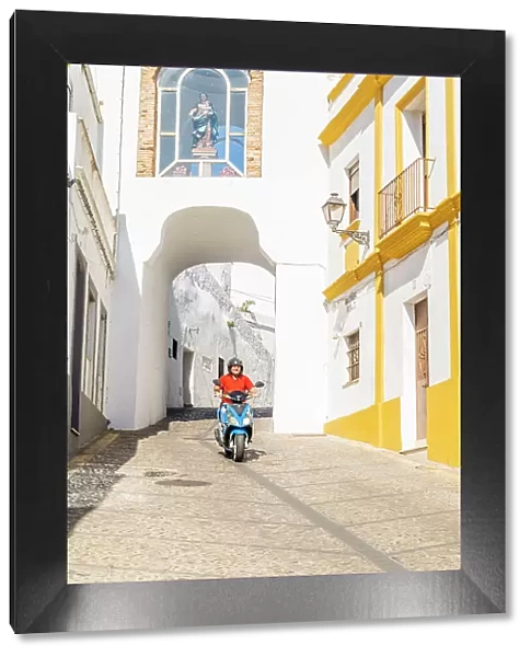 Man riding a scooter through Puerta de Matrera, Arcos de la Frontera, Andalusia, Spain