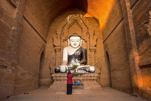 Bagan, Mandalay region, Myanmar (Burma). Woman praying at the Buddha in a huge temple