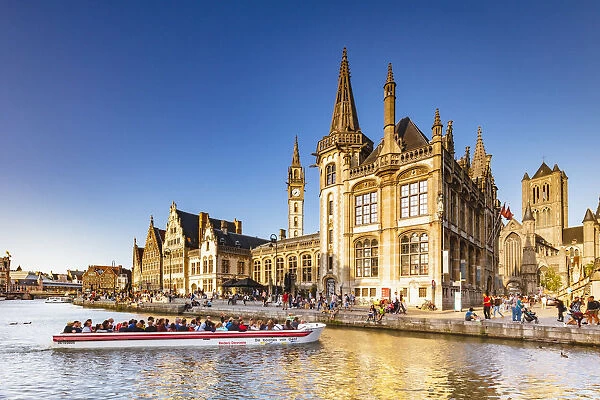 A boat with tourists on the canal with the Ghent town buildings reflecting at sunset