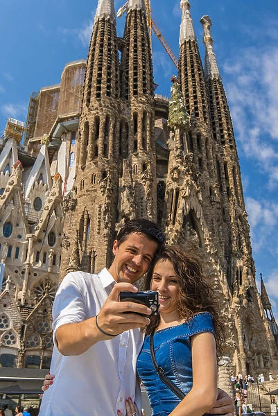 Caucasian young couple taking photo of themselves in front of Sagrada Familia church