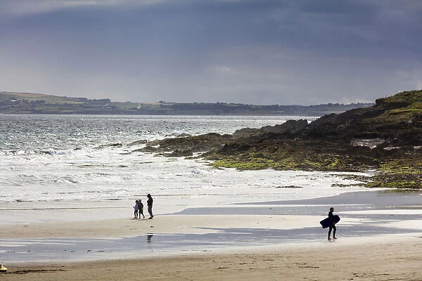 Europe, Kinsale, a surfer and toursits at sunset on the beach near Laherne Hill