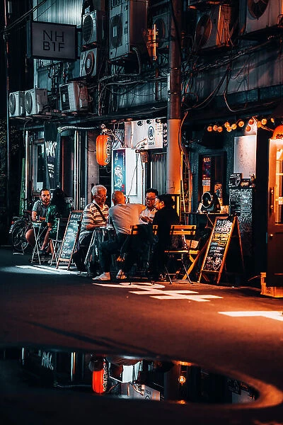 Friends chat and drink at a table in the streets of Osaka at night. Japan