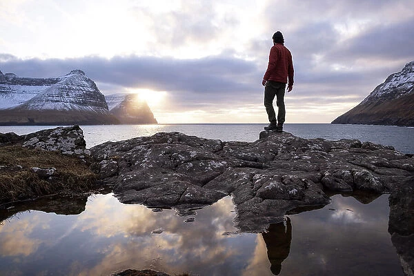 A guy standing on the coast in Viðareiði at sunset. Island of Viðoy. Faroe Islands