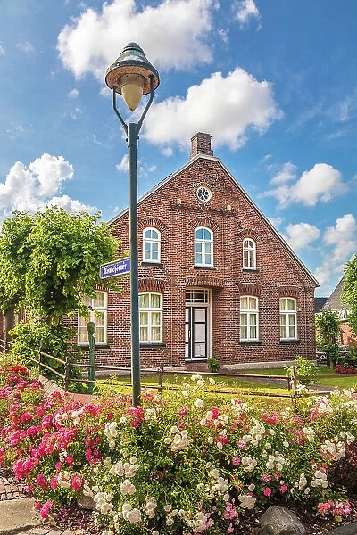 Historic brick house and lush floral decorations in the village of Rysum, Krummhoern, East Frisia, Lower Saxony, Germany