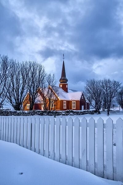 The illuminated church at dusk in the cold snowy landscape at Flakstad Lofoten Norway
