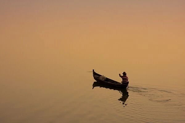 Myanmar, Burma, Amarapura. A fisherman paddling across Taungthaman Lake at sunrise