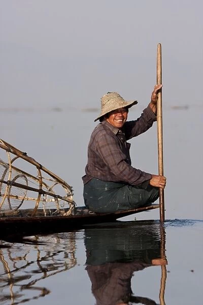 Myanmar, Inle Lake. Intha fisherman gently paddling his boat across Inle Lake, Myanmar