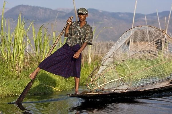 Myanmar, Inle Lake. Intha fisherman with traditional conical fish net, gently paddling his flat-bottomed