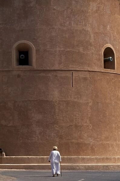 An old Omani man walks beneath the imposing watchtower