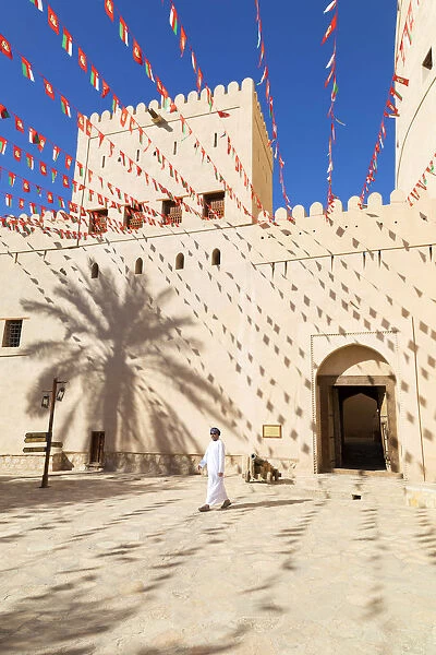 An Omani man walks past Bahla Fort decorated to celebrate the birthday of Sultan Qaboos