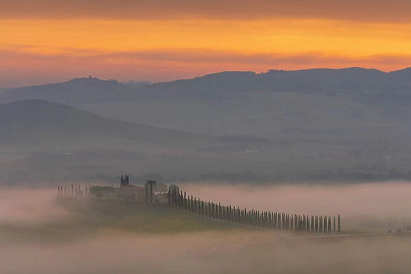 Poggio Covili rising through the thick morning fog during a misty spring sunrise. Val d'Orcia, Tuscany, Italy