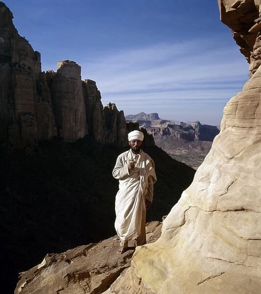 A priest stands outside the rock-hewn church of Abune