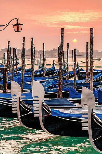 Romantic sky at dawn over gondolas moored side by side on St Mark's waterfront, Venice, Veneto, Italy