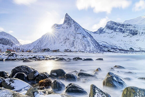 Rorbu on frozen Ersfjord beach with snowy Hatten mountain on background, Senja island, Troms county, Norway