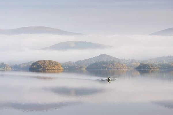Single sculler rowing across a misty Derwent Water at dawn, Lake District, Cumbria, England