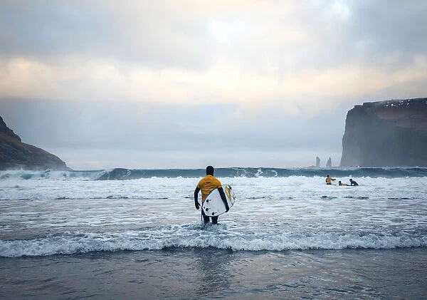 A surfer on the sandy beach of Tjornuvik walking towards the ocean. Streymoy, Faroe Islands