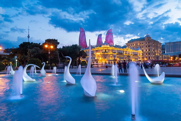 A swans fountain in the Baki Bulvari with Flame Towers in the background at twilight
