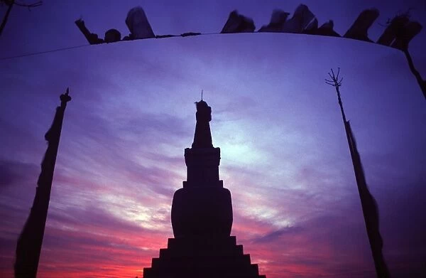 Tibetan Buddhist stupa and prayer flags silhouetted against sunset
