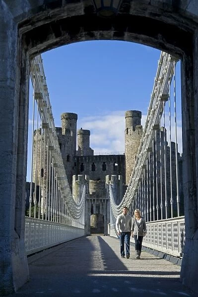 UK, North Wales; Conwy. Couple on the elegant Suspension Bridge built by Thomas Telford across the Conwy River to the imposing