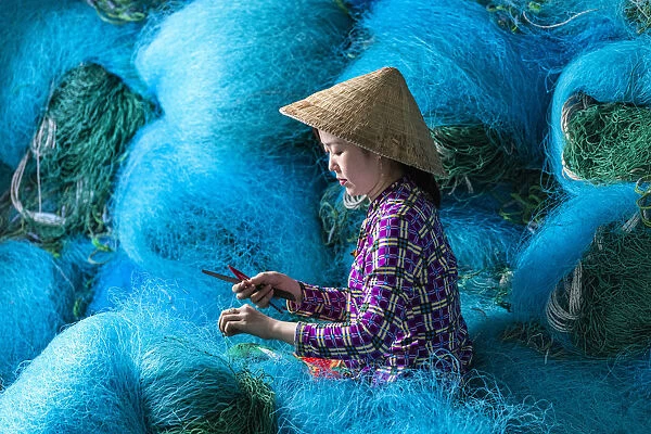 A Vietnamese woman mending blue fishing net, Mekong Delta, Vietnam
