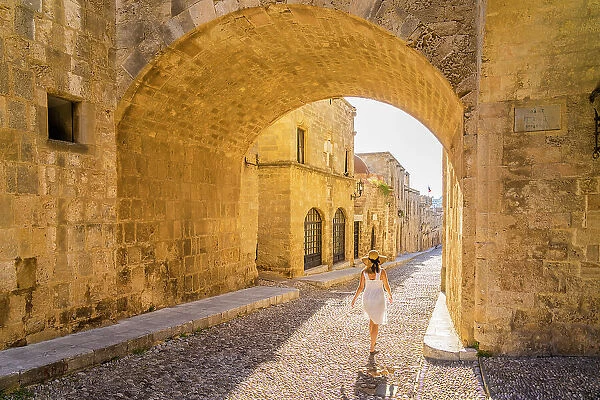 A woman in a hat walking in the Street of the Knights of Rhodes, in the Medieval City of Rhodes, UNESCO, Rhodes, Dodecanese Islands, Greece. (MR)