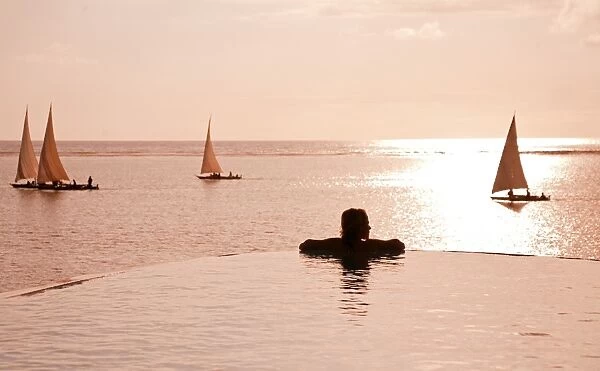 Zanzibar, Matemwe Bungalows. A tourist stands at the edge of an infinity pool watching the Dhows