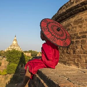 Bagan, Mandalay region, Myanmar (Burma). A young monk with red umbrella watching