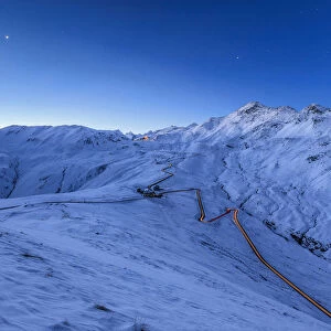 Blue light of dusk on the snowy landscape and the hairpin turns of Stelvio Pass Braulio