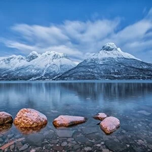 Blue sky at dusk and snowy peaks are reflected in the frozen sea at Oteren Storfjorden Lapland Lyngen Alps Tromsa¸ Norway Europe