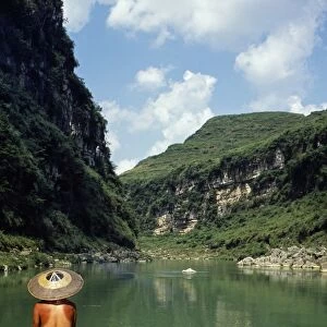 A boatman rows between the hills and cliffs of the Chong an River