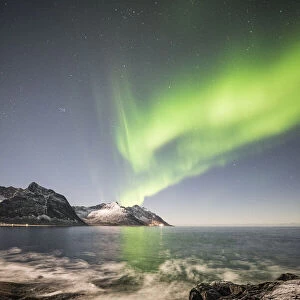 Frozen sea and rocky peaks illuminated by Northern Lights, Tungeneset, Senja, Tromso