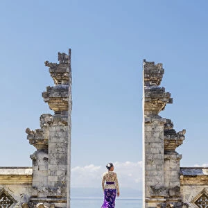 Indonesia, Bali, Candidasa. A local young woman standing in the gateway to the Pura