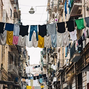 Man walks in an alley in Naples, with clothes hanging between the buildings