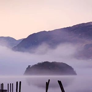Old wooden jetty and St Herberts Island on Derwent Water at dawn on a misty