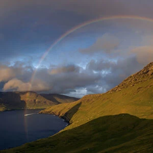 A full rainbow at sunset over the cliffs in Vagar. Faroe Islands