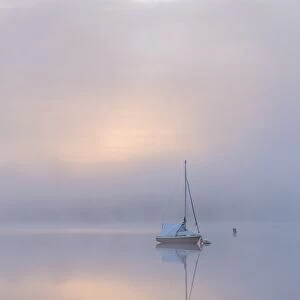 Sailing boat in misty conditions at dawn on a reflective Wimbleball Lake, Exmoor National Park