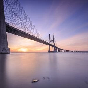 The sun rises on the Vasco da Gama Bridge that spans the Tagus River in Parque das NaA'A§A'Aµes Lisbon Portugal Europe