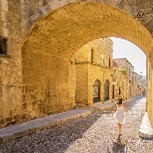 A woman in a hat walking in the Street of the Knights of Rhodes, in the Medieval City of Rhodes, UNESCO, Rhodes, Dodecanese Islands, Greece. (MR)