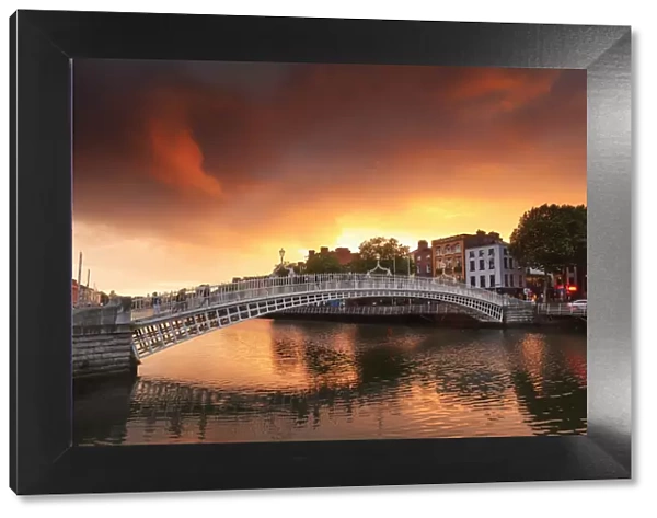 Europe, Dublin, Ireland, people crossing Halfpenny bridge on the Liffey river at sunset