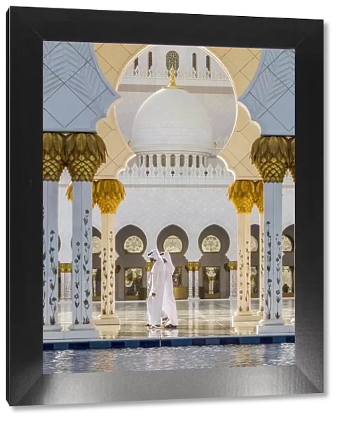 Two Middle Eastern men traditionally dressed walking in the courtyard of the Sheikh Zayed Mosque