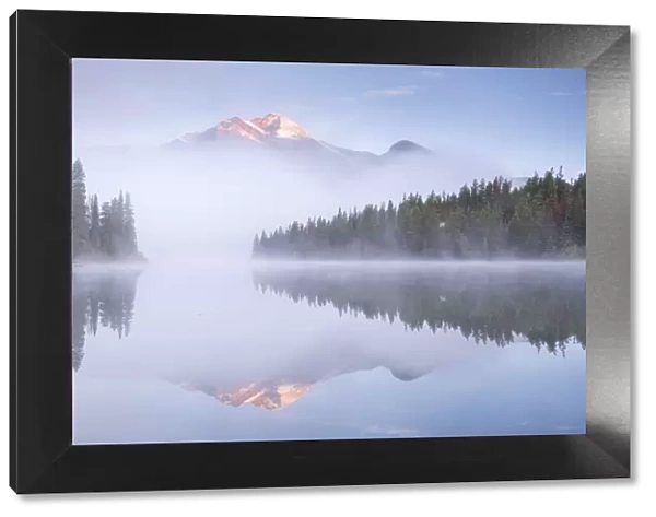 A mist shrouded Pyramid Mountain reflected in Pyramid Lake at dawn, Jasper National Park