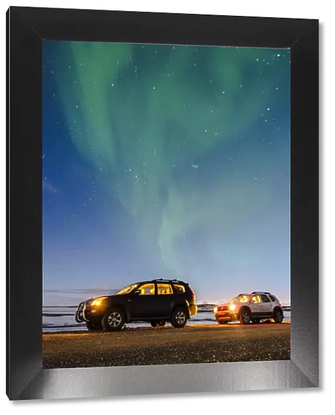 Iceland, Europe. Cars with lights on at night under a starry sky and the northern lights